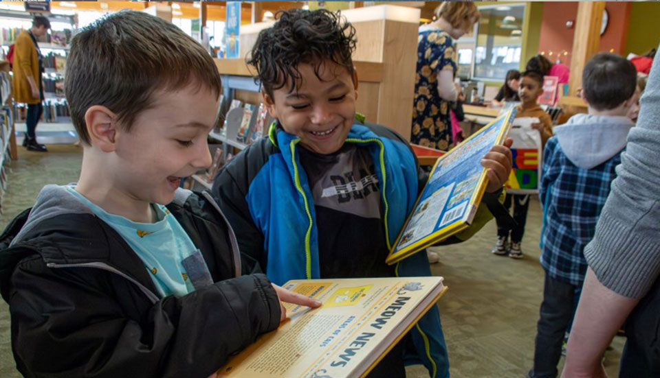 two kids looking at a book and laughing