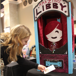Woman taking paper from a booth labeled "The Amazing Libby"
