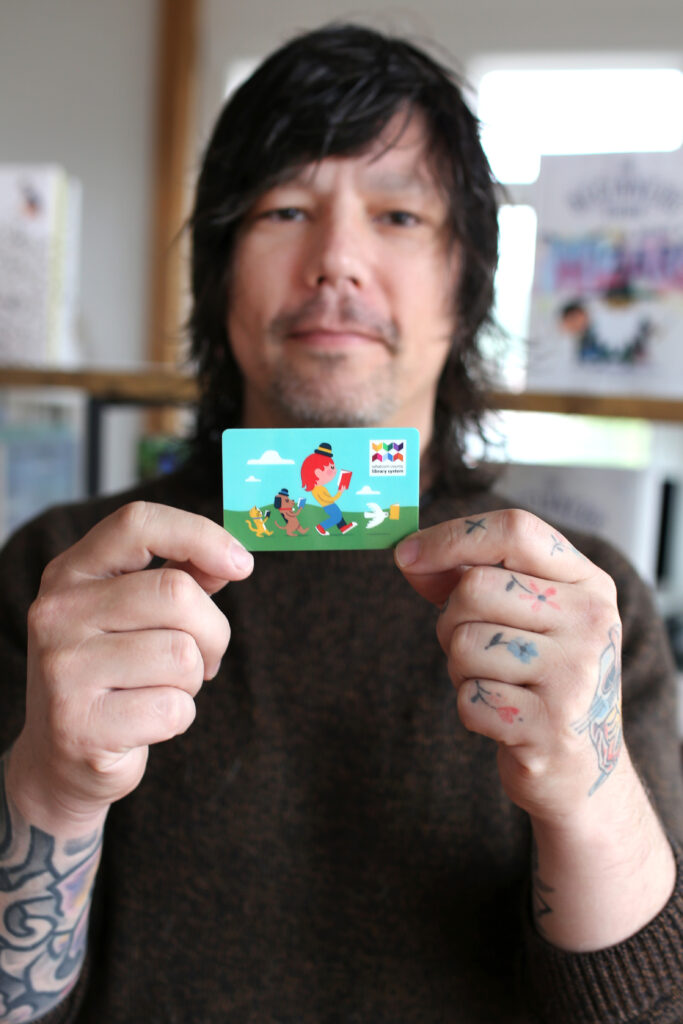 Keith Negley holding a library card he designed.