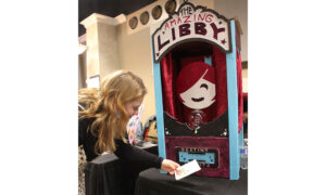 Woman feeding a piece of paper into a slot on a fortune teller machine that says The Amazing Libby
